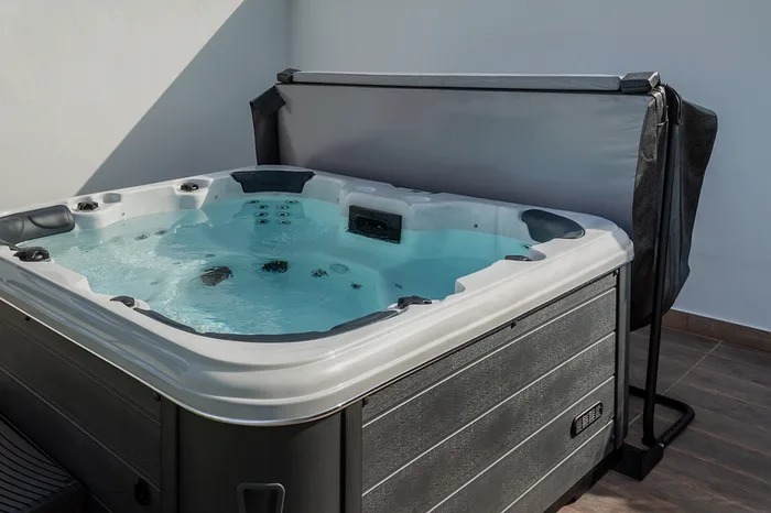 Black hot tub cover lift holding a spa cover open, revealing a modern outdoor hot tub with bubbling water.